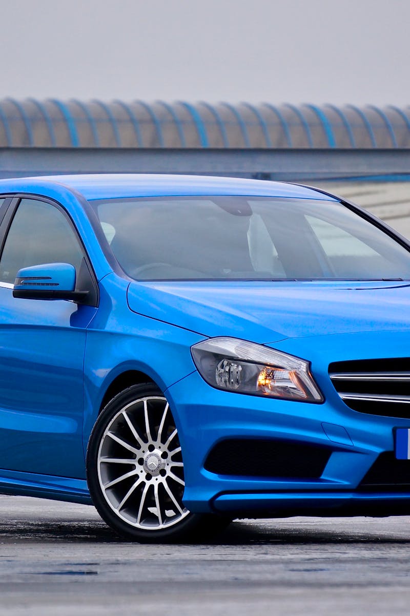 Vehicle Insurance Elegant blue Mercedes-Benz hatchback parked outdoors with a modern architectural backdrop.